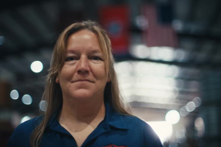 A proud female American worker in a factory warehouse turns to smile confidently at the camera