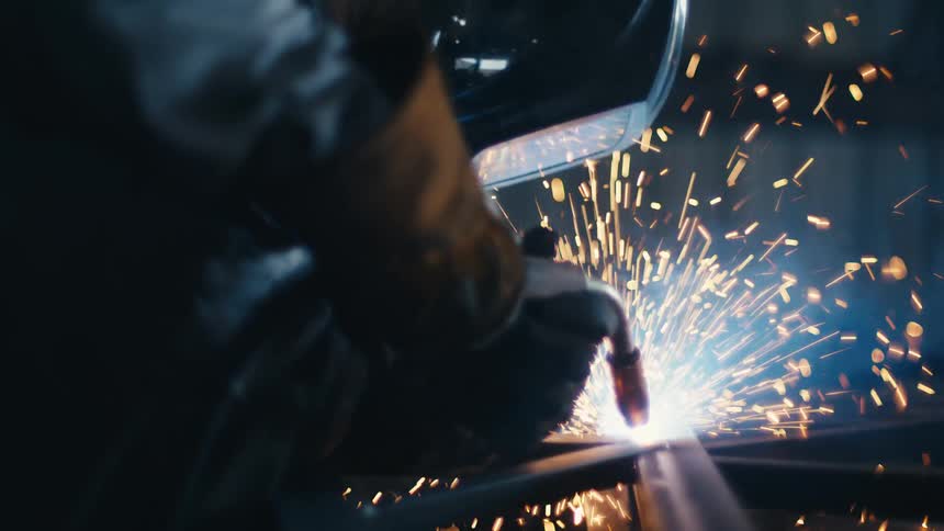 Close-up slow-motion shot of a welder fusing metal, with bright blue light and orange sparks flying