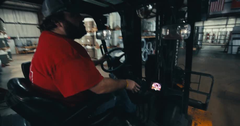 Over the shoulder shot of a factory worker driving a forklift through a large industrial warehouse