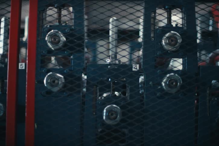 A close-up view of automated industrial machinery with spinning rollers operating on a production line behind a safety fence