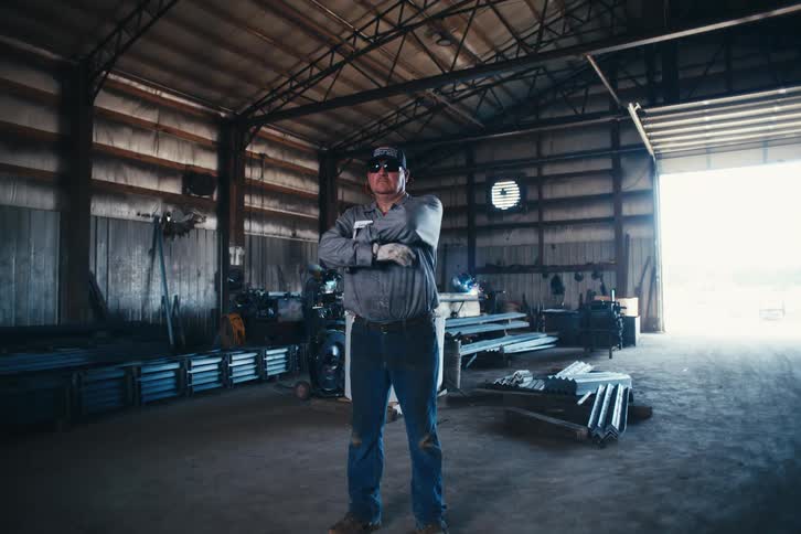Portrait of a confident blue-collar worker crossing his arms in a bustling metal fabrication shop