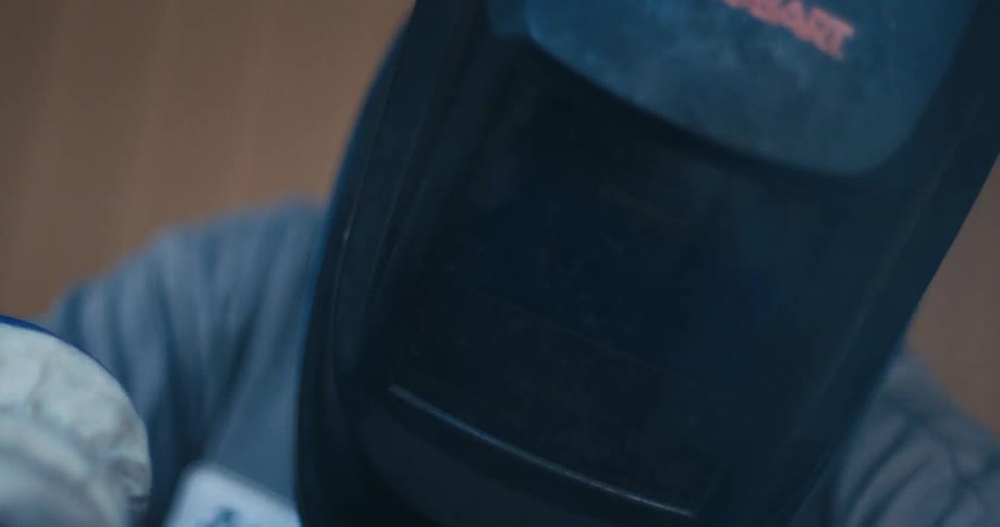 Artistic slow-motion close-up of a welder's helmet with glowing sparks flying by, creating a beautiful bokeh effect