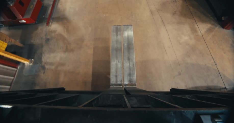 High-angle point-of-view from a forklift reversing through an industrial warehouse