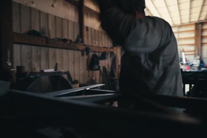 A welder creates a shower of sparks while working on a metal frame in an industrial workshop before lifting his mask