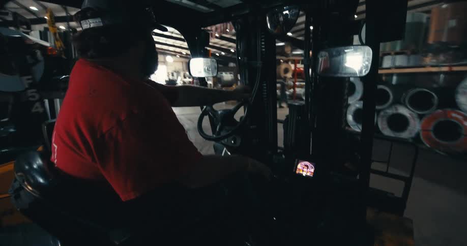 A forklift operator skillfully maneuvers through a bustling industrial warehouse filled with large metal spools