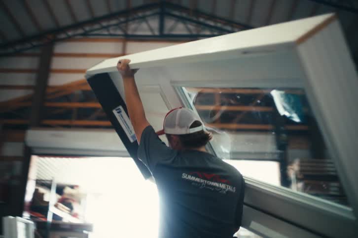 A factory worker carries a large, newly manufactured white door through a warehouse in slow motion