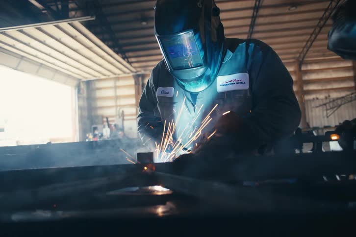 Dramatic slow-motion shot of a welder in a protective mask creating a shower of sparks while working on metal in a workshop