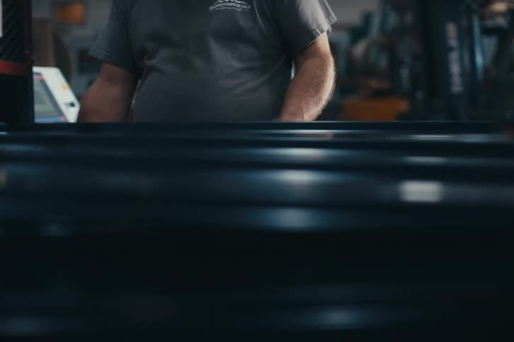 Close-up of a metal fabrication machine pressing and shaping black corrugated sheets on a production line in a factory