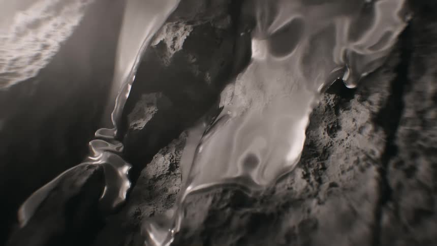 A mysterious, silvery liquid metal oozes and flows over a dark, rocky terrain in a dramatic black and white closeup