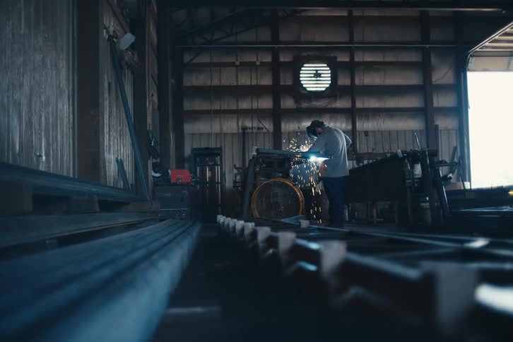 A metalworker in a dimly lit workshop uses a grinder, sending a shower of bright sparks into the air