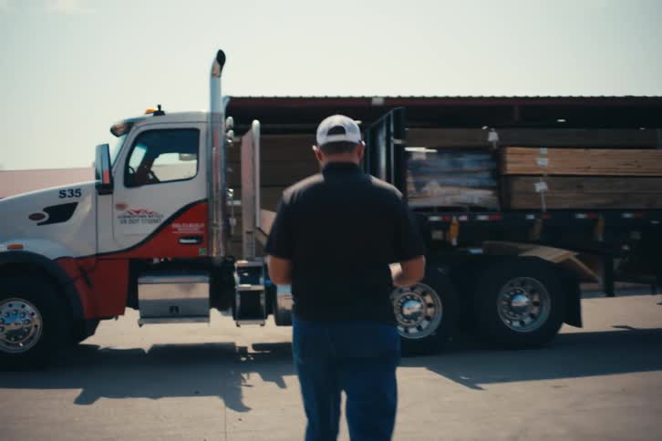 A man walks in slow motion toward a semi-truck loaded with lumber at an industrial yard