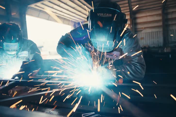 Slow-motion close-up reveals two welders creating a shower of sparks while working on a metal structure in a workshop