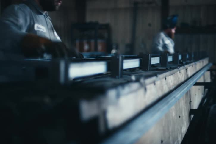 A skilled metalworker carefully positions a long steel truss on a production line in an industrial workshop
