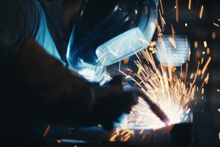 Slow motion close-up of a welder meticulously joining metal as a shower of brilliant sparks illuminates the dark workshop
