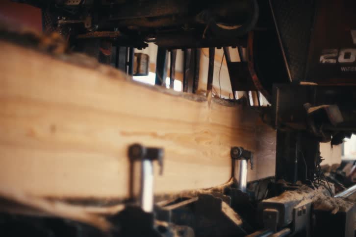 Slow motion close-up of an industrial bandsaw cutting a large log at a sawmill