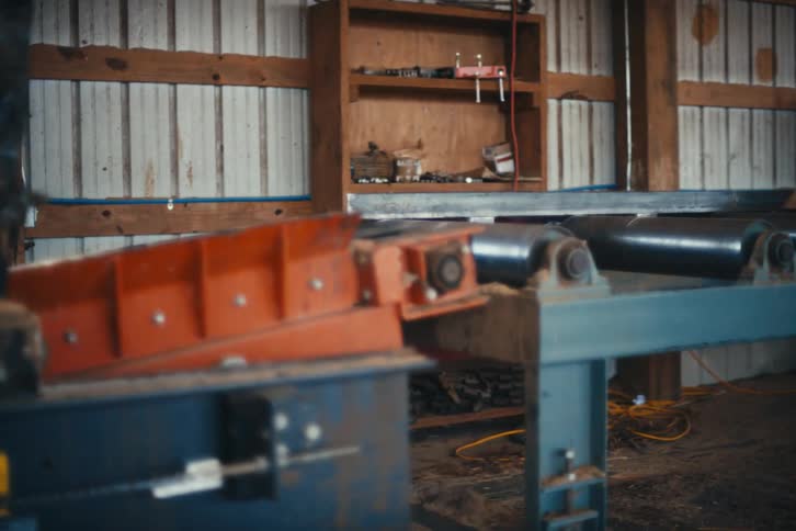 Blurry, handheld shot panning across an industrial sawmill with heavy machinery and a worker in the background