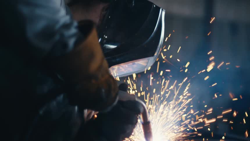 A skilled welder meticulously joins metal with a torch, creating a spectacular display of light and sparks in a dark workshop