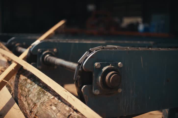 Close-up shot of a conveyor belt at a sawmill moving a large log for processing