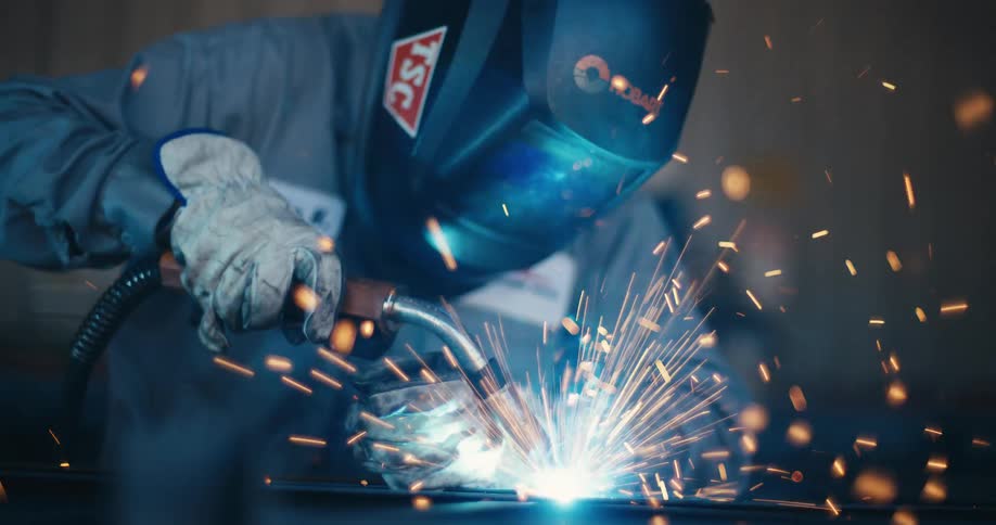 Close-up in slow motion of a welder wearing a protective mask creating a brilliant shower of sparks while working on metal