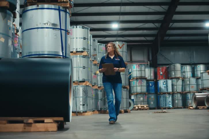 Slow motion shot of a woman taking inventory of large steel coils in an industrial warehouse