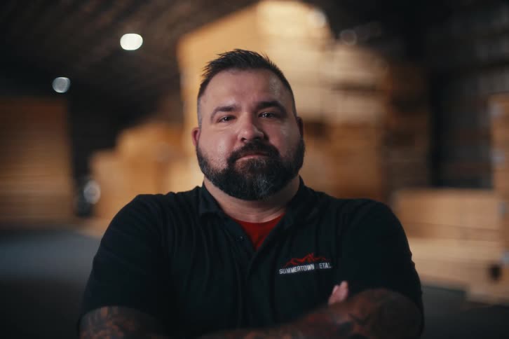 Close-up portrait of a serious, tattooed blue-collar worker crossing his arms in a warehouse