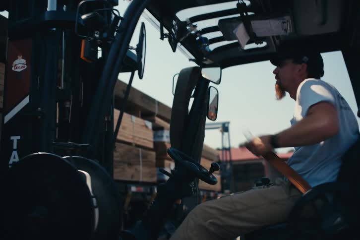 A lumberyard worker gets into his forklift and buckles up to begin his workday in slow motion