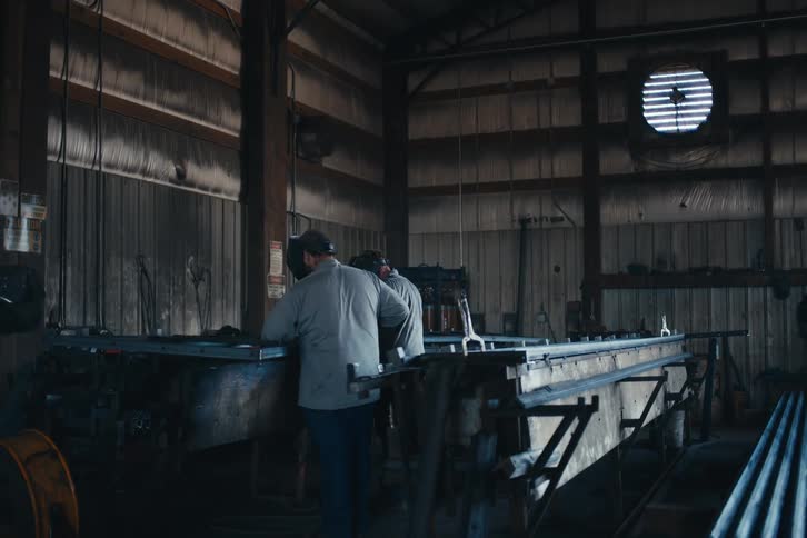 Two workers weld a large metal frame in an industrial workshop as sparks fly