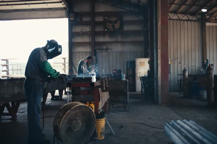 Two industrial welders work diligently in a fabrication shop, with sparks flying from their torches