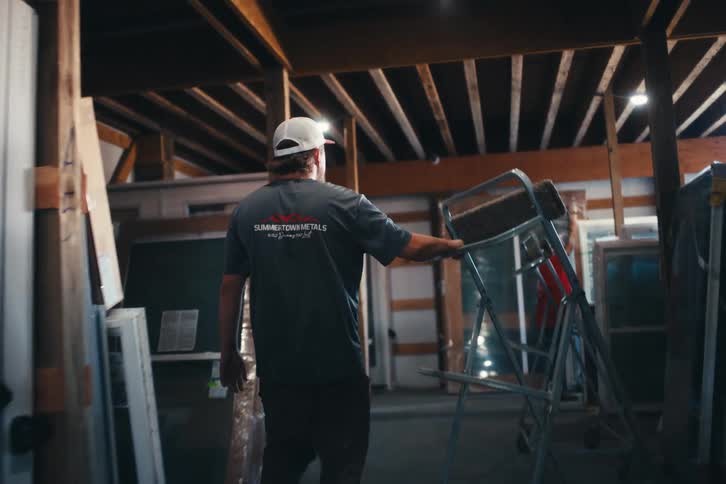 A worker pushes a cart through a dimly lit warehouse filled with doors and windows in slow motion