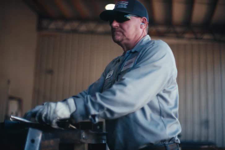 A blue-collar worker in a metal fabrication shop meticulously assembles parts at his workstation in slow motion