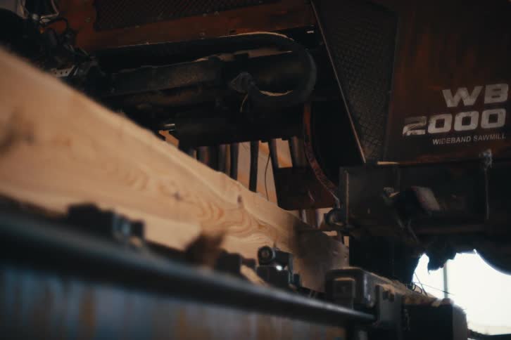 An industrial wideband sawmill precisely cuts a thick wooden plank in a busy workshop