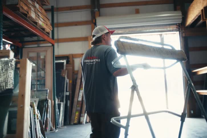 Slow motion shot following a male construction worker carrying a sawhorse through a large warehouse