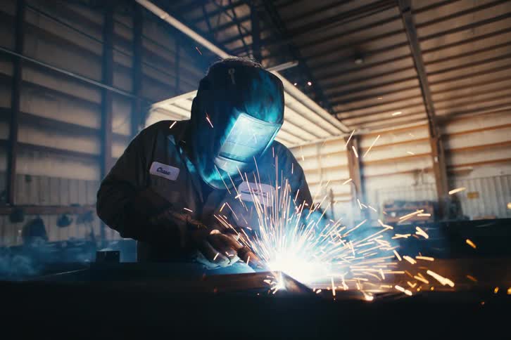 Dramatic slow-motion close-up of a welder in a protective mask working with metal as bright sparks fly