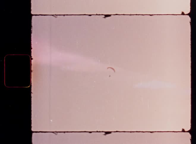 Vintage 8mm film scan shows a lone paraglider floating peacefully in a hazy, warm-toned sky