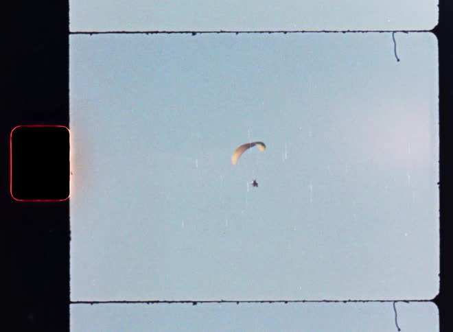 Vintage 8mm footage captures a solitary paraglider soaring through the open sky
