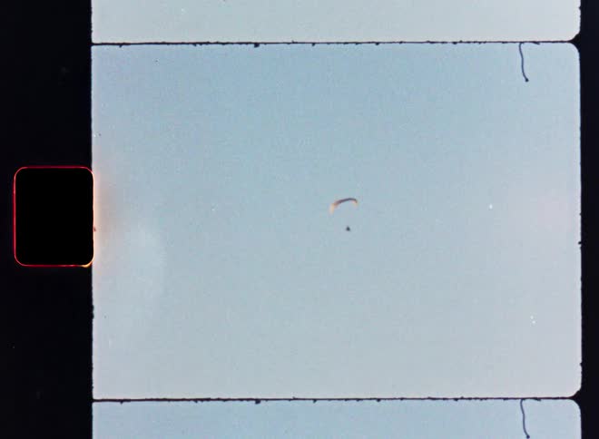 A lone paraglider soars through the vast, open sky in a vintage 8mm film scan with light leaks and grain