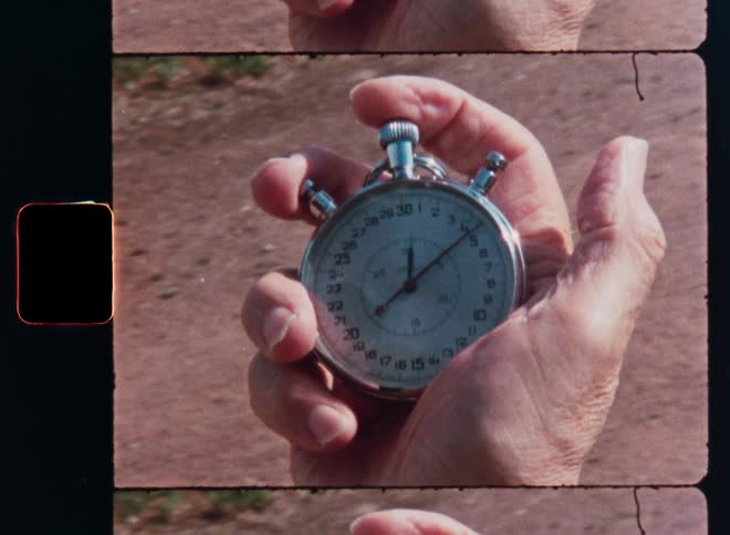 A close-up on vintage film of a hand holding and starting an analog stopwatch