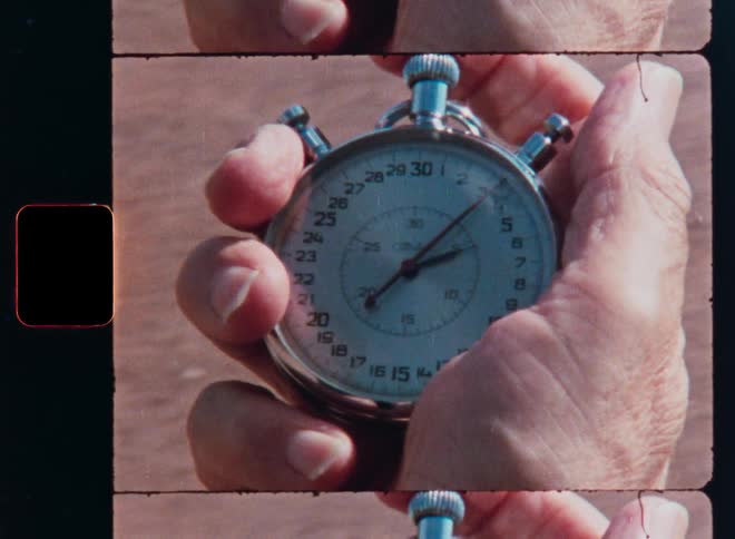 Close up of a hand holding and starting an analog stopwatch, shot on grainy vintage film