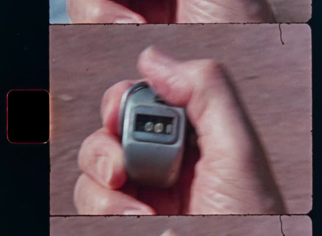 A close-up of a person's hand clicking a mechanical tally counter from zero to one, shot on vintage film