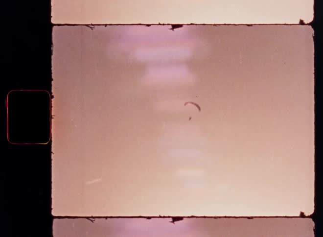 Vintage 8mm film scan shows a lone paraglider soaring peacefully through a warm, hazy sky