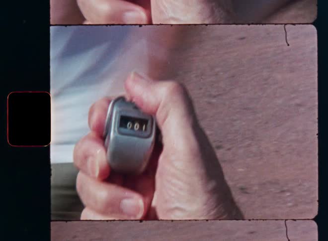 A close-up shot on vintage 8mm film of a hand clicking a mechanical tally counter from zero to one
