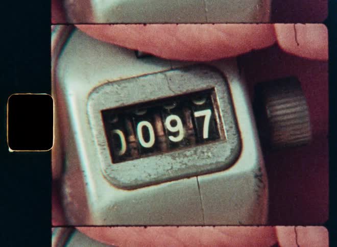 A person's hand clicks a vintage mechanical tally counter, advancing the numbers from 90 to 100 in a close-up, grainy, film-style shot
