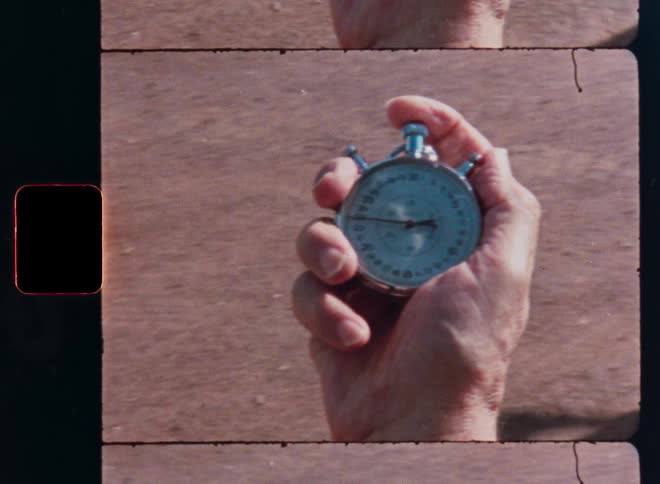 A close-up shot on vintage film of a hand starting a classic analog stopwatch as a runner passes by