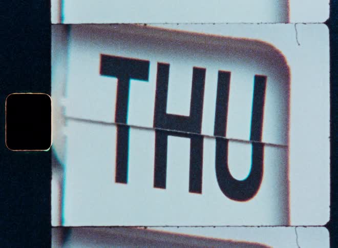 A close-up of a retro flip clock rapidly cycling through the days of the week, shot on vintage film
