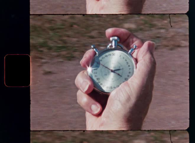 Archival film captures a close-up of a hand clicking start on a classic analog stopwatch