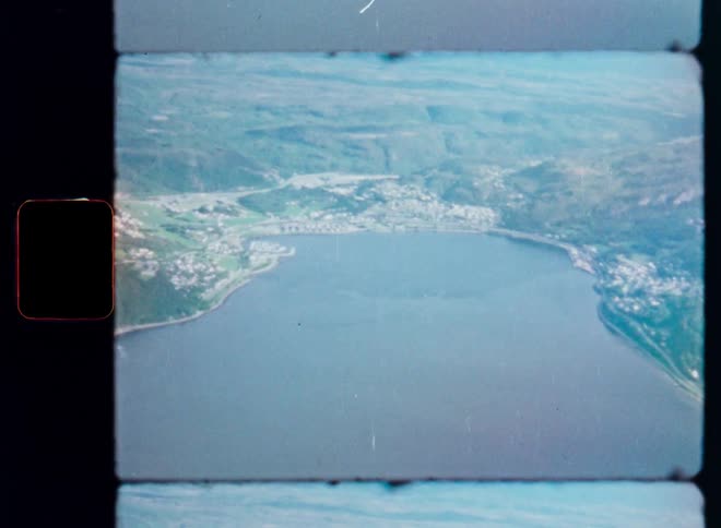 Archival Super 8mm footage provides a nostalgic aerial view of a coastal European town nestled in a bay surrounded by green hills