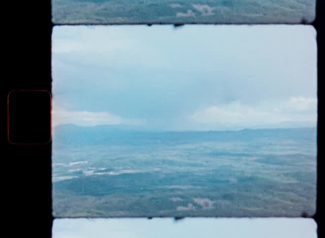 Vintage 8mm footage captures a dramatic rainstorm pouring down over a vast, forested landscape as seen from an airplane window