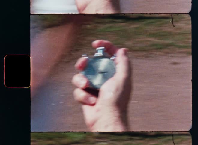 Vintage film strip footage shows a close-up of a hand holding an analog stopwatch during a running race