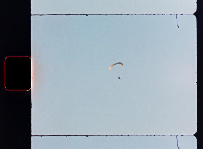 A lone paraglider soars across the vast open sky in this vintage 8mm film scan