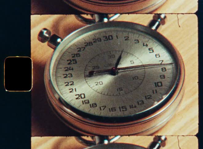 A vintage silver stopwatch ticks away the seconds on a classic 8mm film strip with visible sprockets